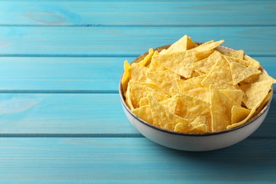 Photo of Tortilla chips (nachos) in bowl on light blue wooden table. Space for text