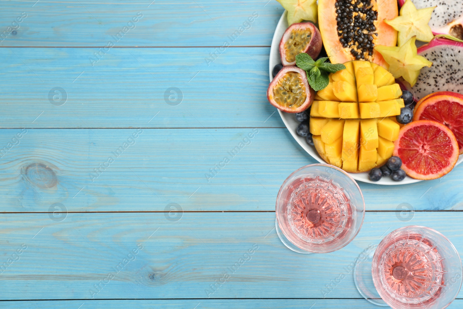 Photo of Delicious exotic fruits and wine on light blue wooden table, flat lay. Space for text