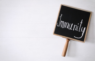 Photo of Chalkboard with word Immunity on white wooden table, top view. Space for text