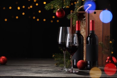 Photo of Bottles of wine, glasses, wooden boxes, fir twigs and red Christmas balls on table, space for text