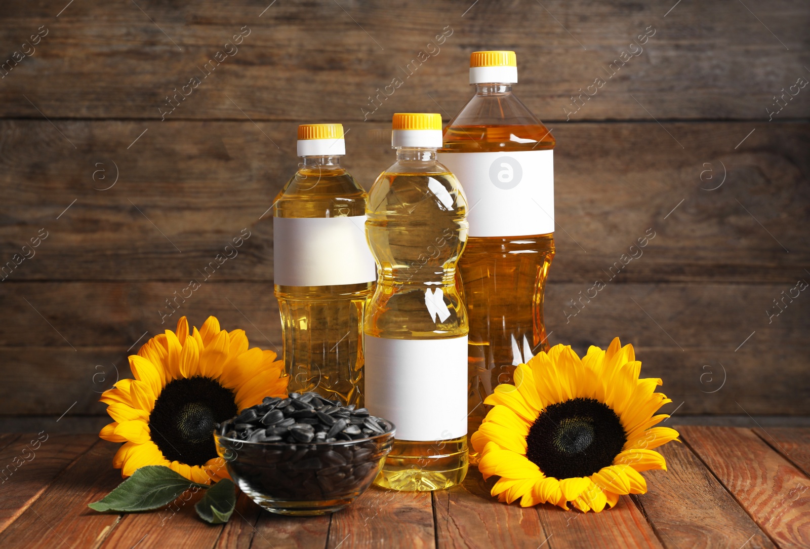 Photo of Sunflower cooking oil, seeds and yellow flowers on wooden table