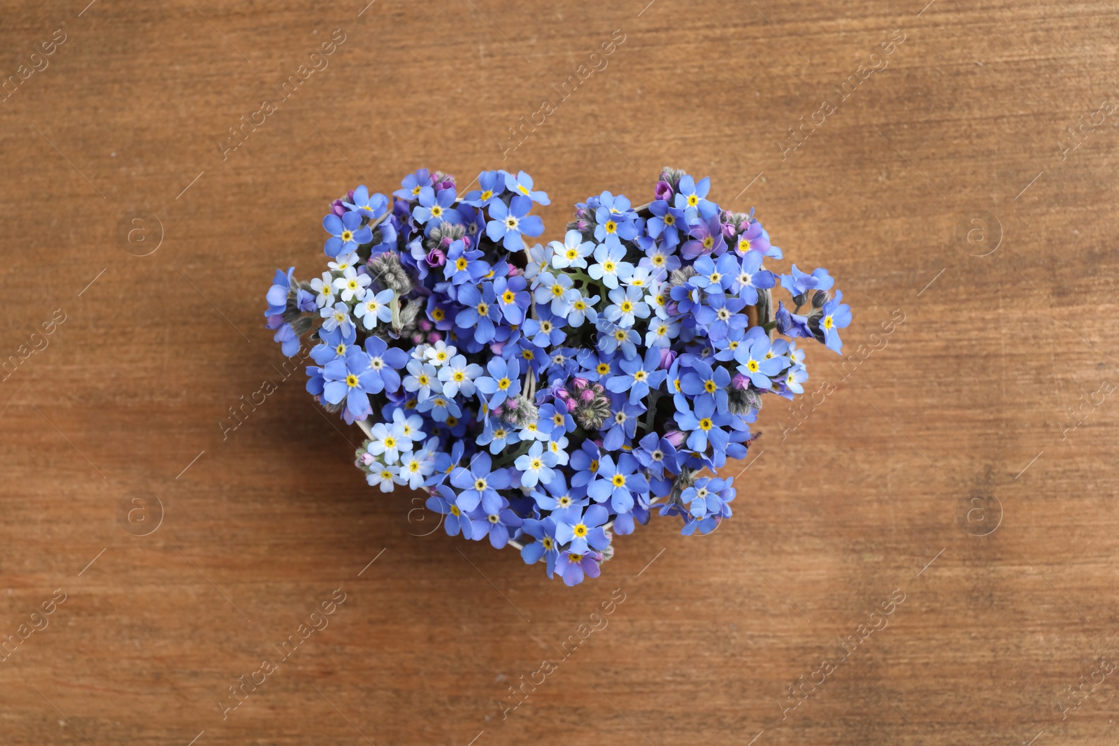 Photo of Heart of beautiful blue forget-me-not flowers on wooden table, top view