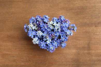 Photo of Heart of beautiful blue forget-me-not flowers on wooden table, top view