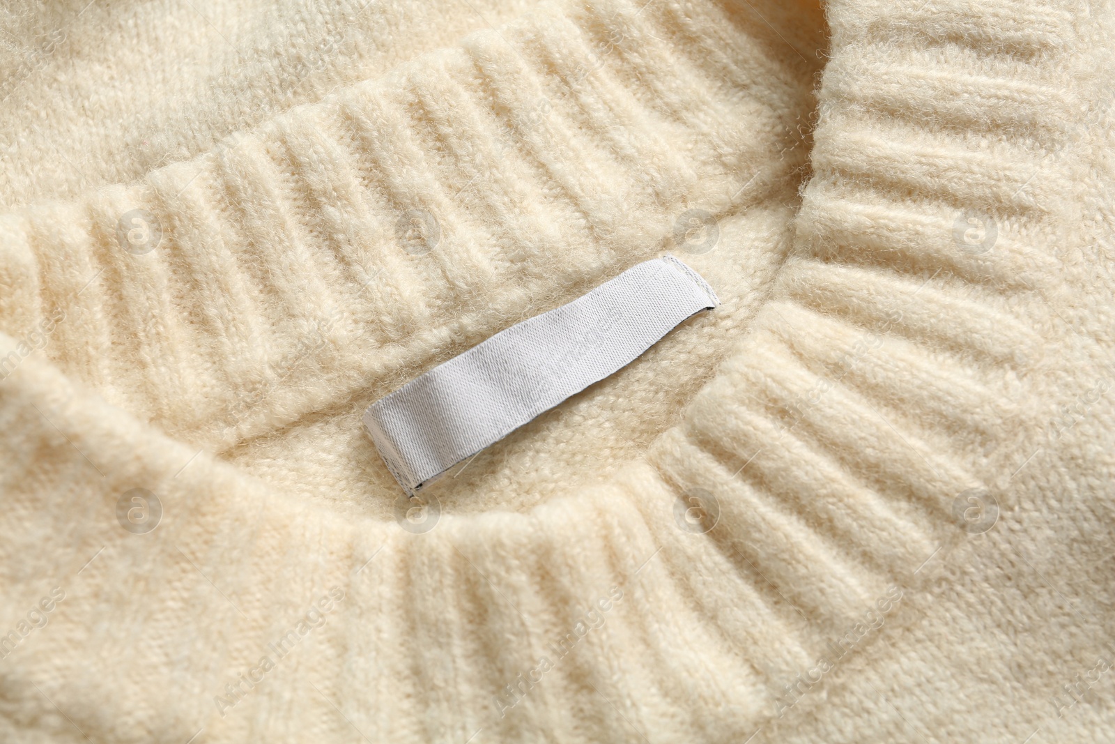Photo of Blank clothing label on white cashmere sweater, top view
