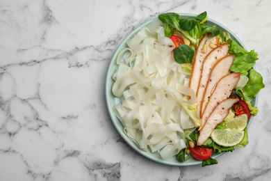 Tasty cooked rice noodles with chicken and vegetables on white marble table, top view