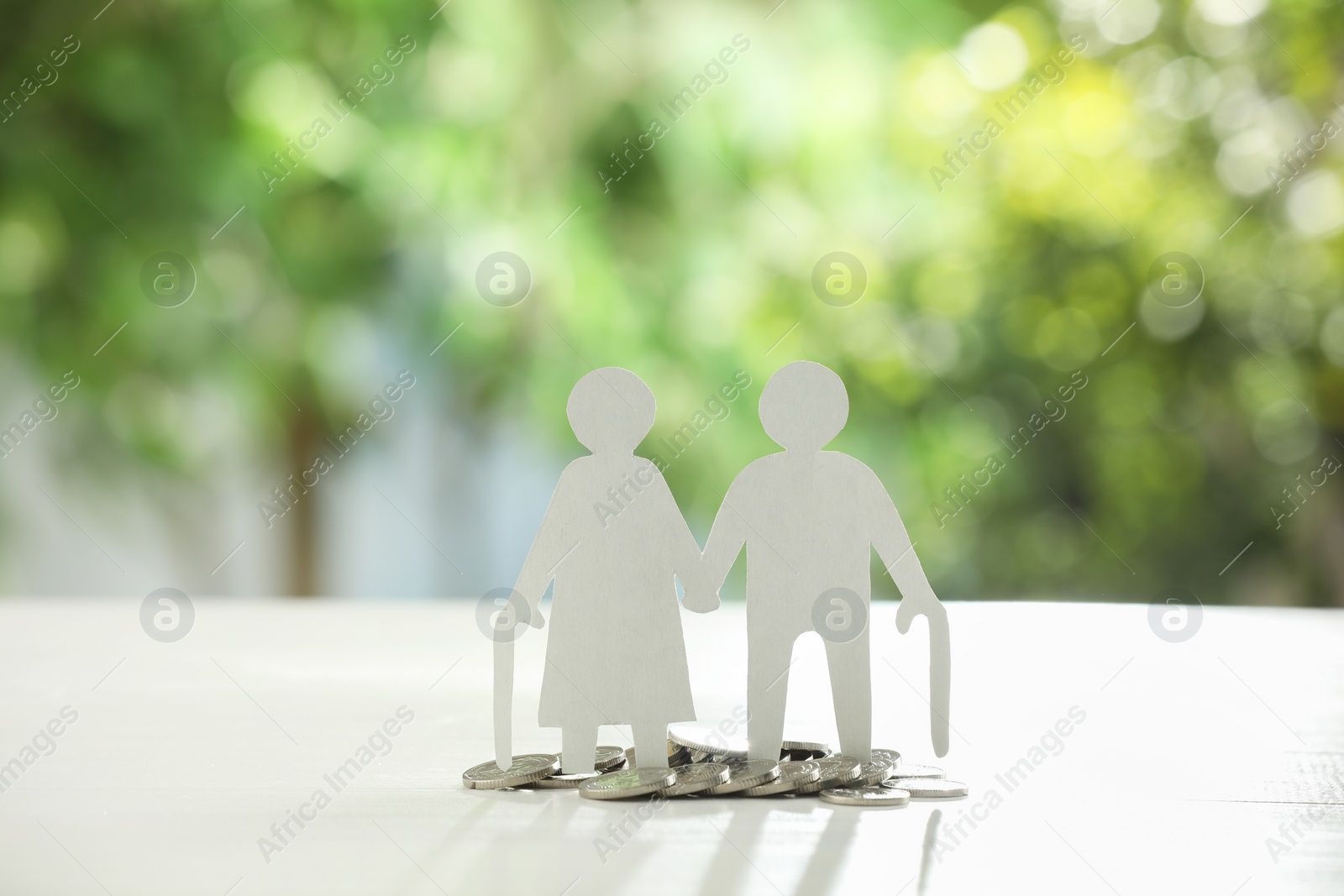 Photo of Pension savings. Figure of senior couple and coins on white table against blurred green background