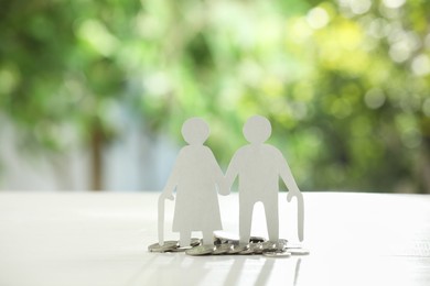 Pension savings. Figure of senior couple and coins on white table against blurred green background