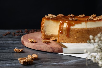 Photo of Sliced delicious cheesecake with caramel and walnuts on black marble table, space for text