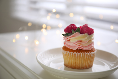 Delicious cupcake with raspberries on table against blurred lights, closeup. Bokeh effect