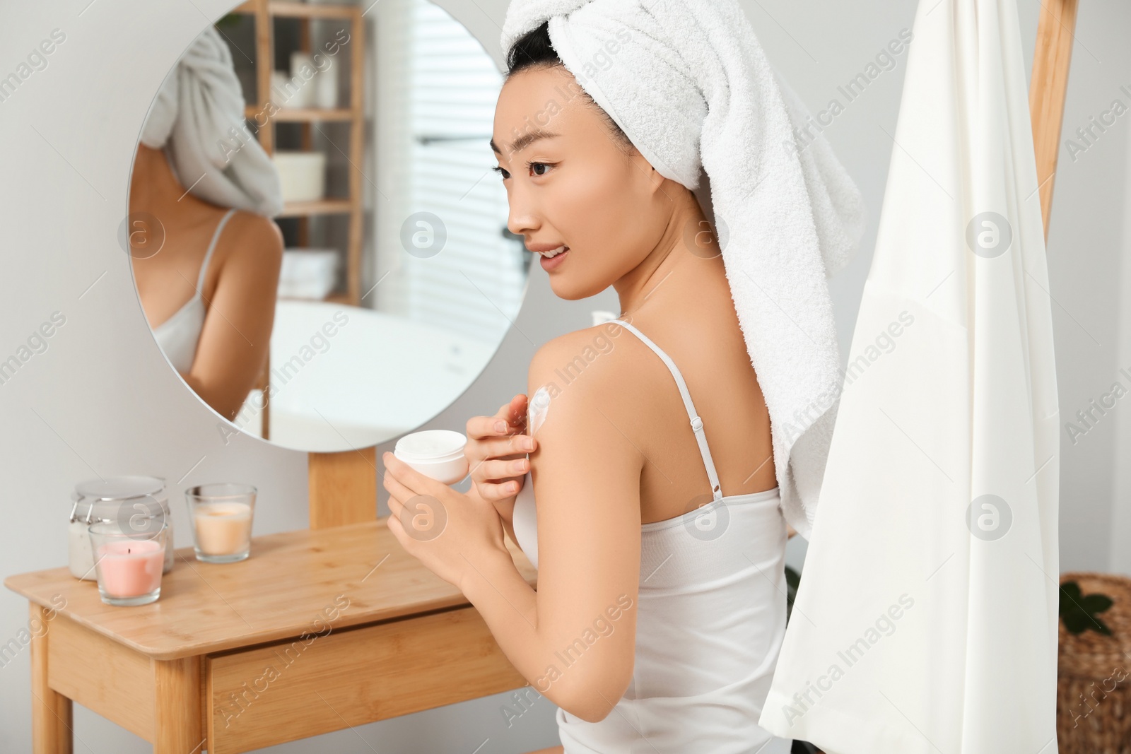 Photo of Beautiful young Asian woman applying body cream on shoulder in bathroom, space for text