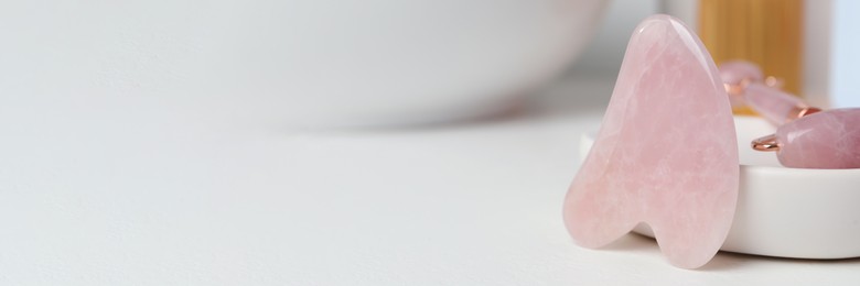 Image of Rose quartz gua sha tool and natural face roller on white table, space for text. Banner design