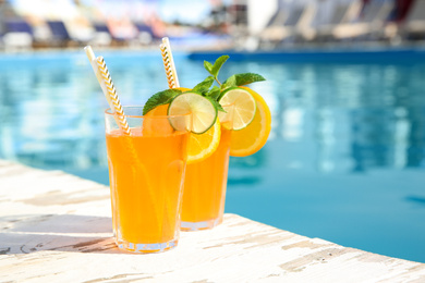 Photo of Refreshing cocktail in glasses near outdoor swimming pool on sunny day. Space for text