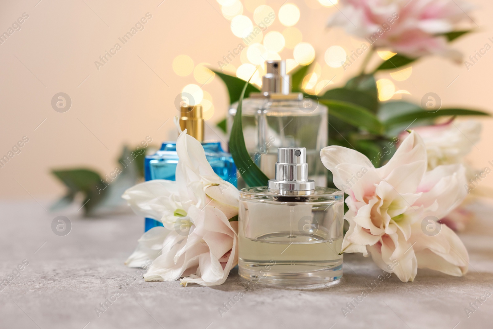 Photo of Bottles of perfume and beautiful lily flowers on table against beige background with blurred lights, closeup