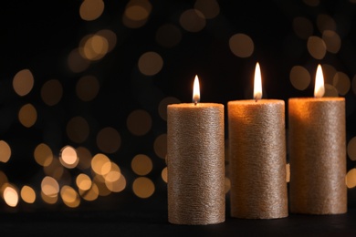 Photo of Burning gold candles against blurred lights in darkness. Space for text