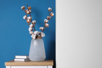 Photo of Cotton branches with fluffy flowers in vase and books on wooden table indoors. Space for text