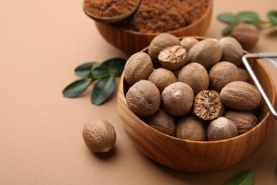 Photo of Nutmeg powder and seeds on light brown background, closeup. Space for text