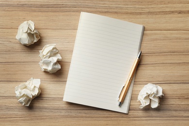 Empty notebook with pen and crumpled paper balls on wooden table, flat lay. Space for text
