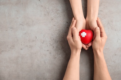 Photo of People holding red heart on gray background, top view with space for text. Cardiology concept