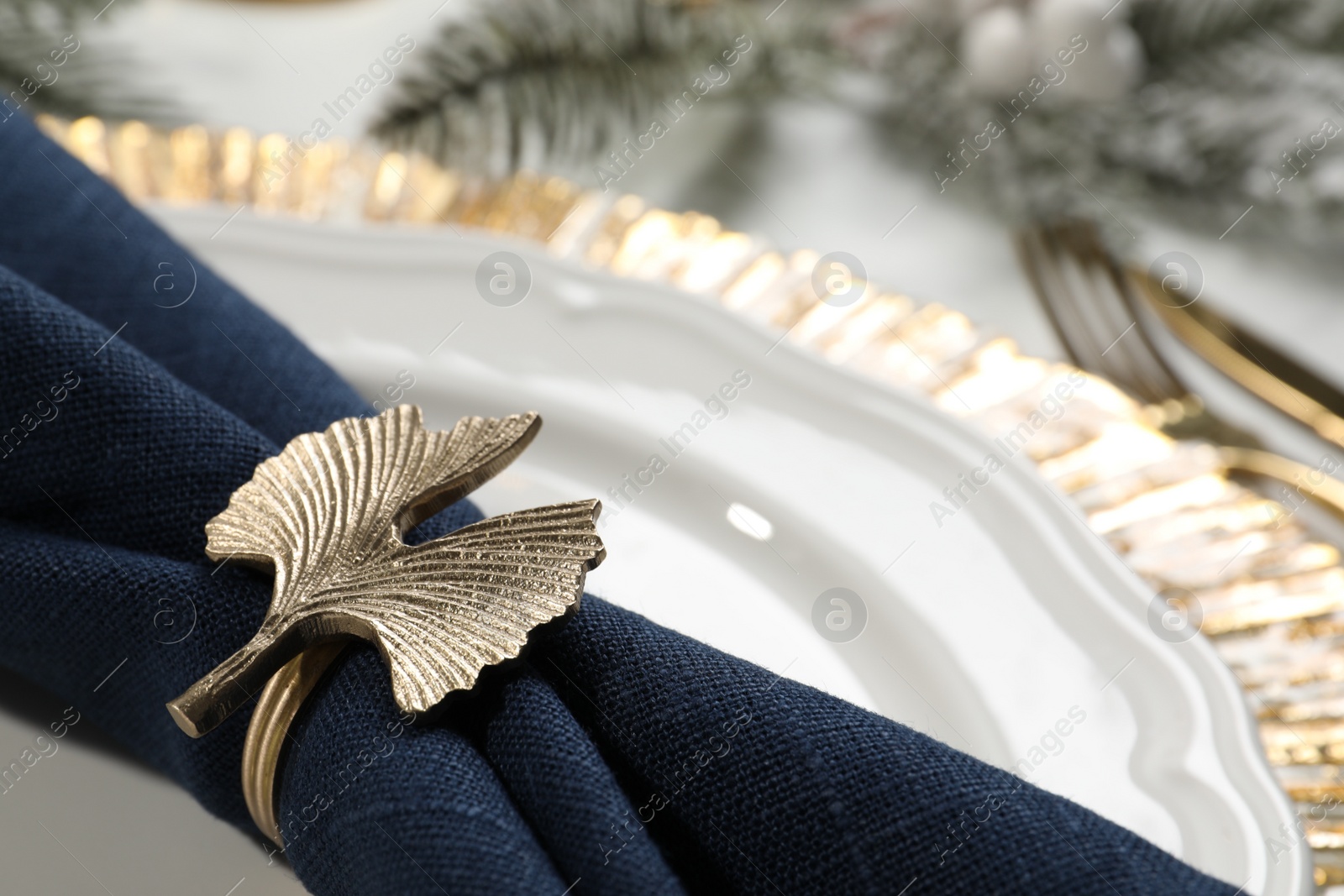 Photo of Dark blue fabric napkin with beautiful decorative ring for table setting on plate, closeup