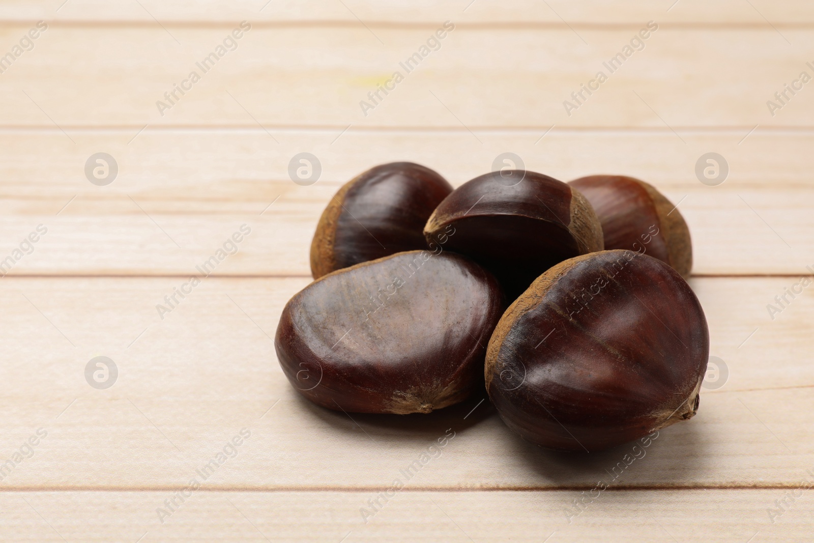 Photo of Sweet fresh edible chestnuts on light wooden table, closeup. Space for text