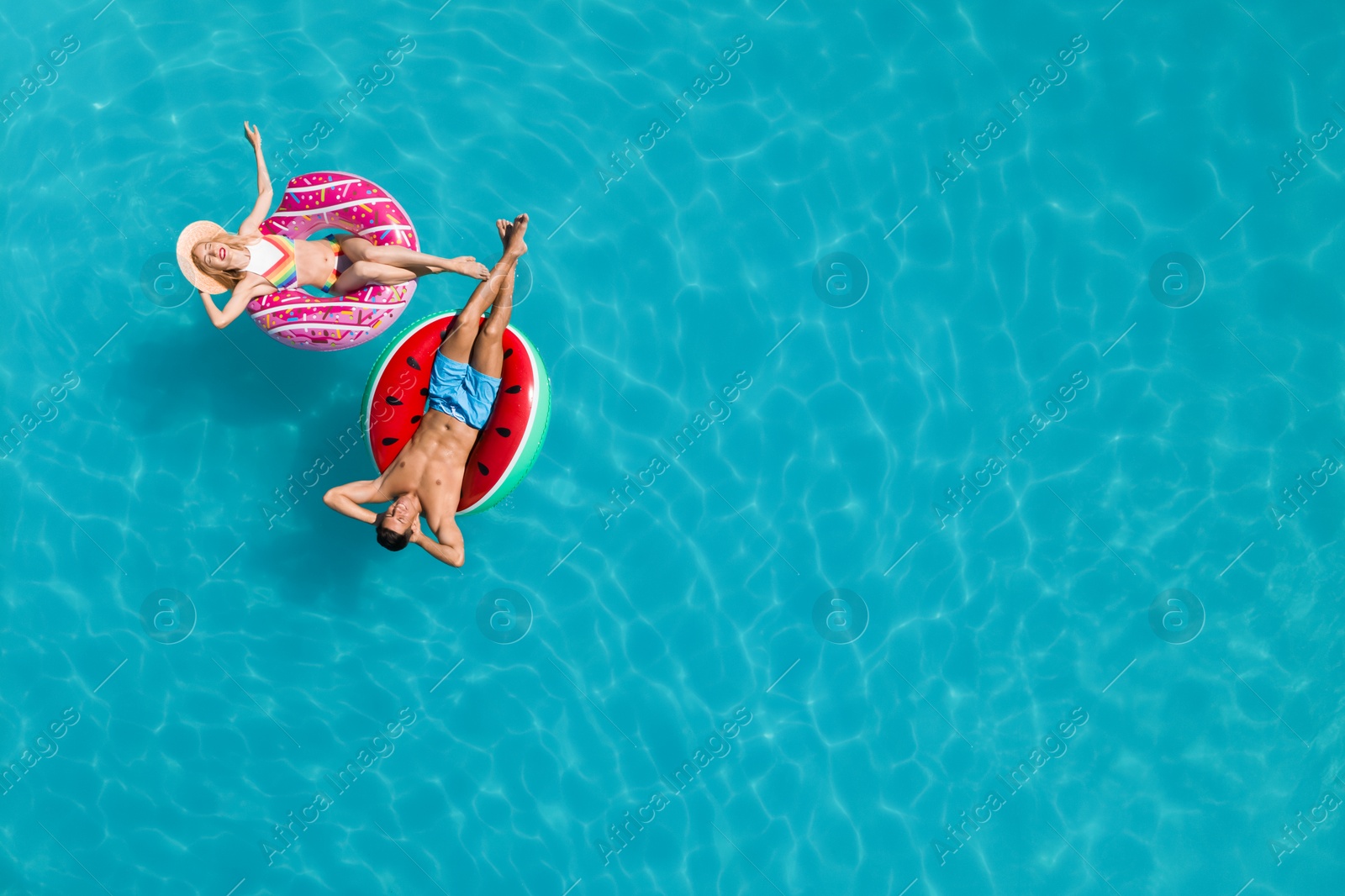 Image of Happy couple with inflatable rings in swimming pool, top view and space for text. Summer vacation