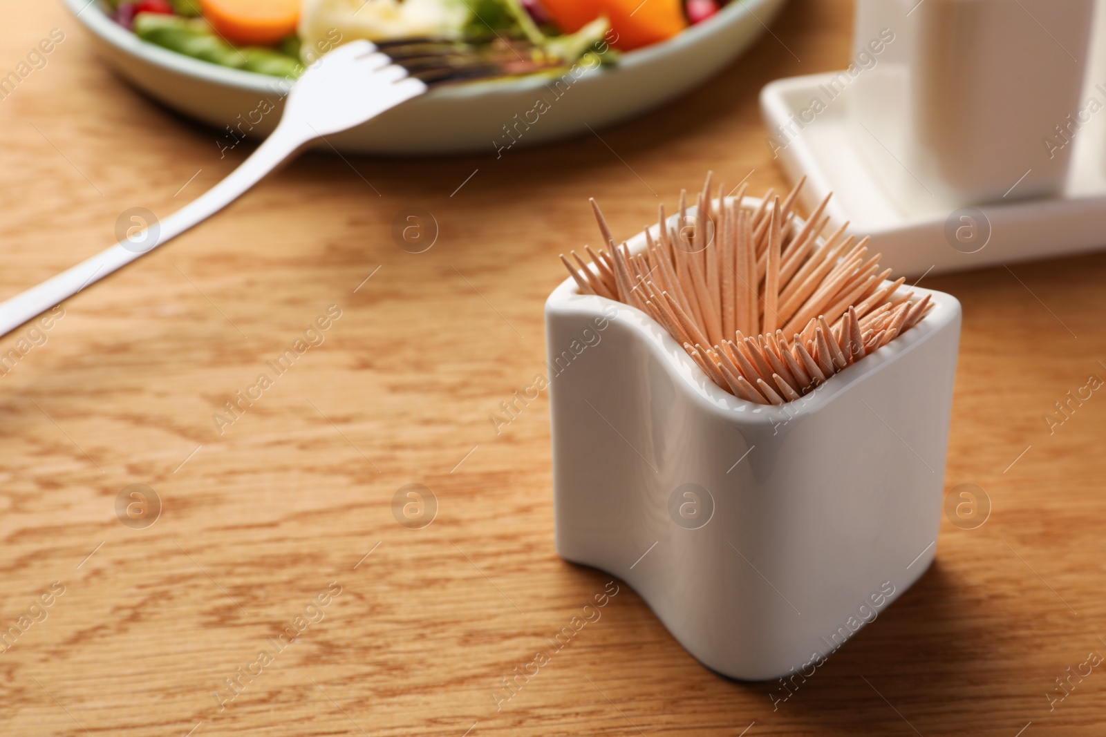 Photo of Holder with many toothpicks on wooden table, closeup. Space for text