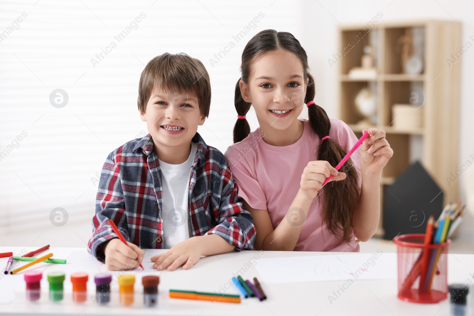 Photo of Happy brother and sister drawing at white table in room