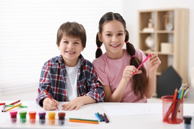 Photo of Happy brother and sister drawing at white table in room