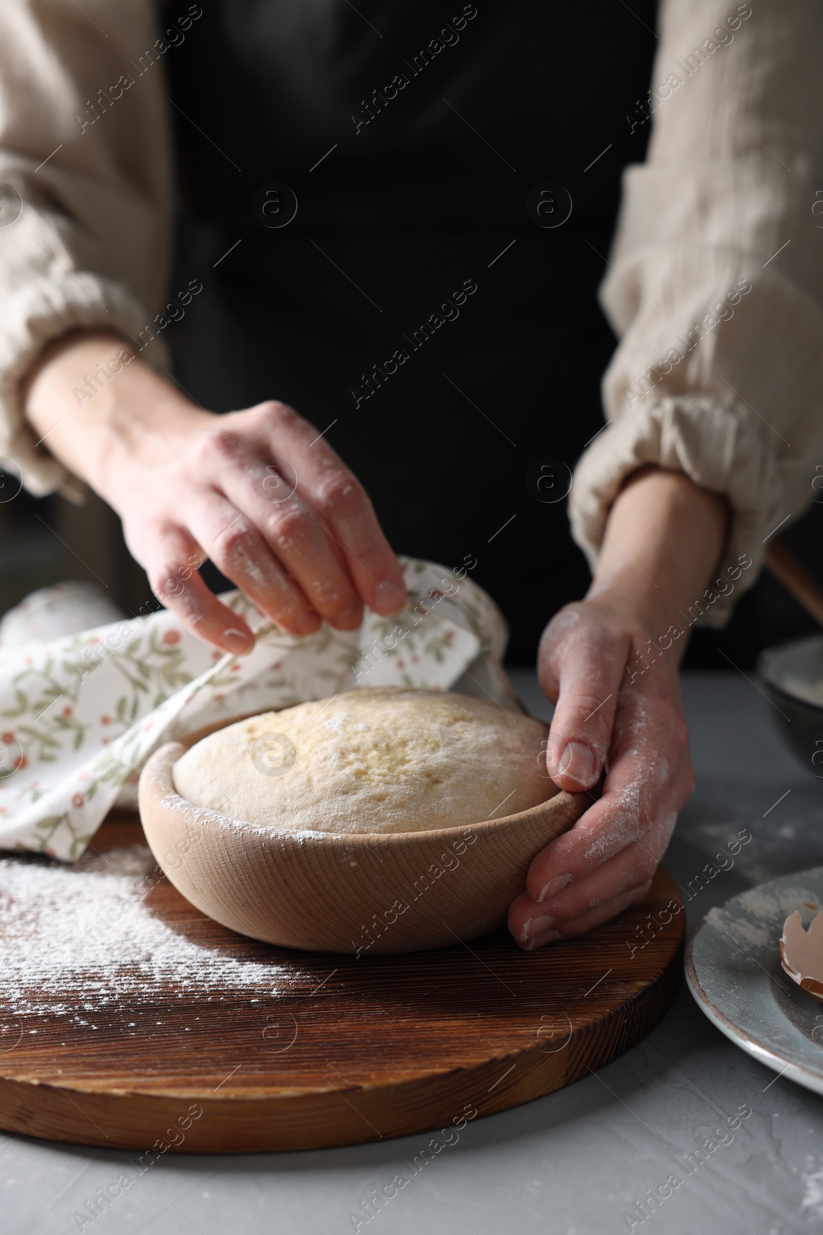 Photo of Woman covering dough with napkin at grey table, closeup