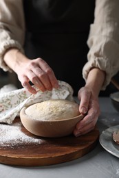 Woman covering dough with napkin at grey table, closeup