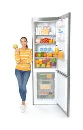 Photo of Young woman with apple near open refrigerator on white background