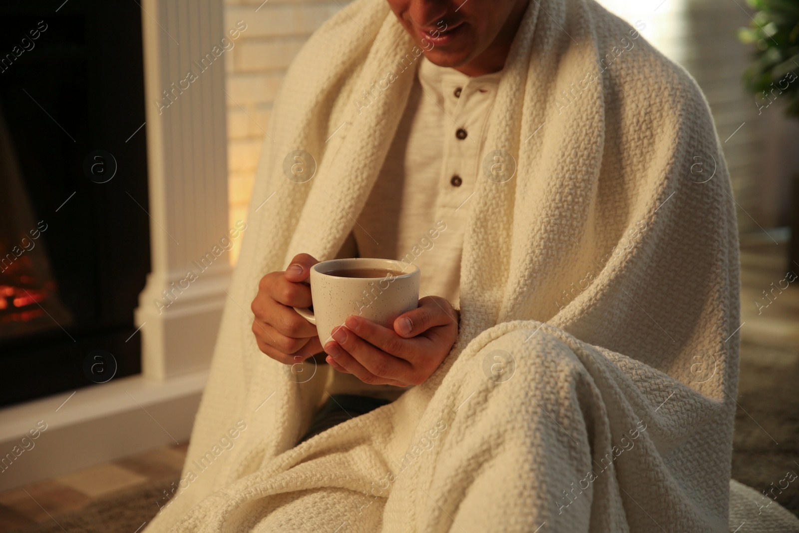 Photo of Man covered with white plaid enjoying cup of tea at fireplace, closeup