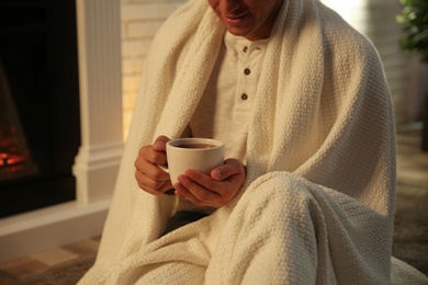 Photo of Man covered with white plaid enjoying cup of tea at fireplace, closeup