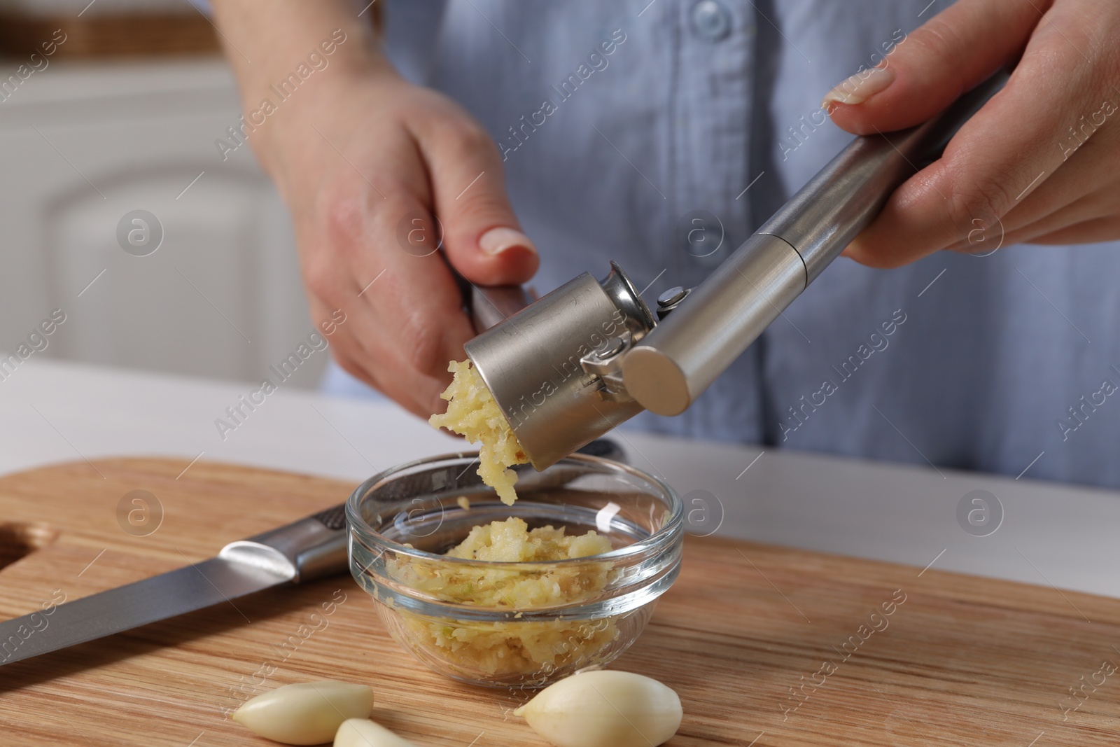 Photo of Woman squeezing garlic with press at wooden table indoors, closeup