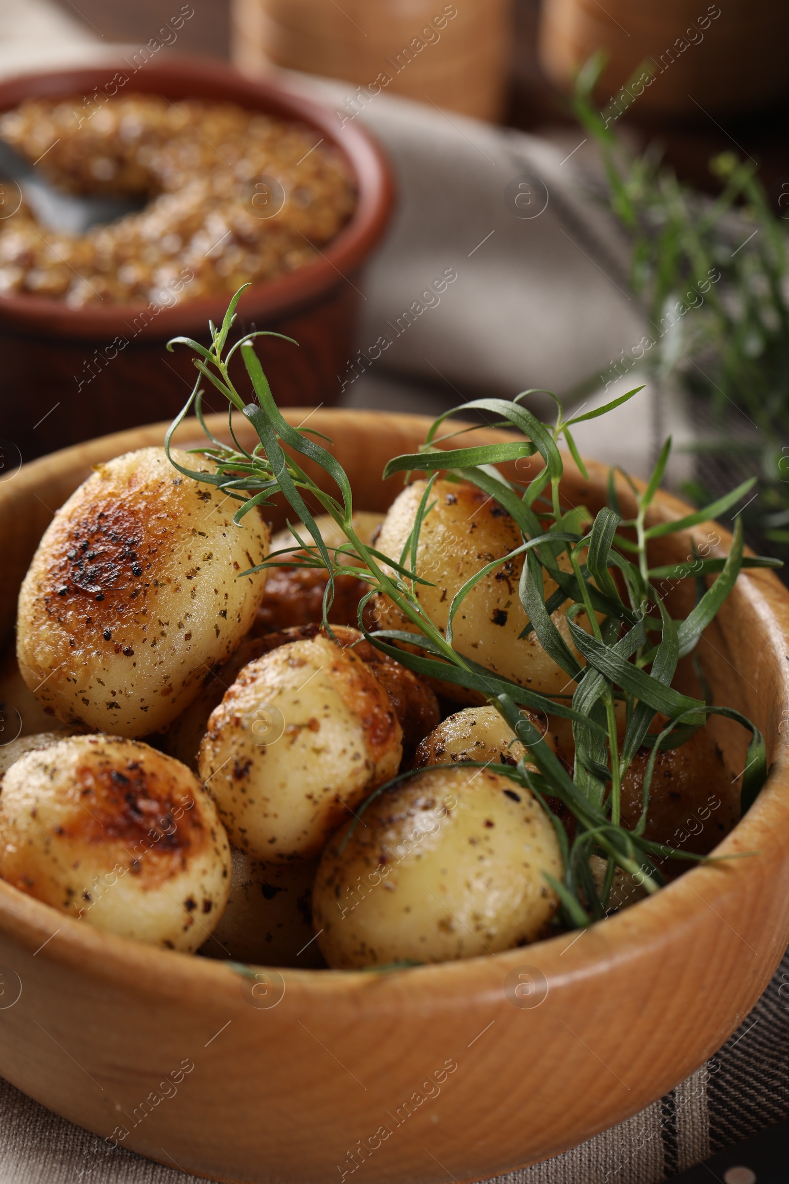 Photo of Delicious grilled potatoes with tarragon in bowl on table, closeup