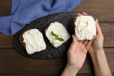 Photo of Woman holding bread with cream cheese at wooden table, closeup