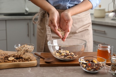 Woman preparing healthy granola bar at grey marble table in kitchen, closeup