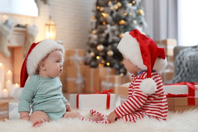 Cute children in Santa hats on floor in room with Christmas tree