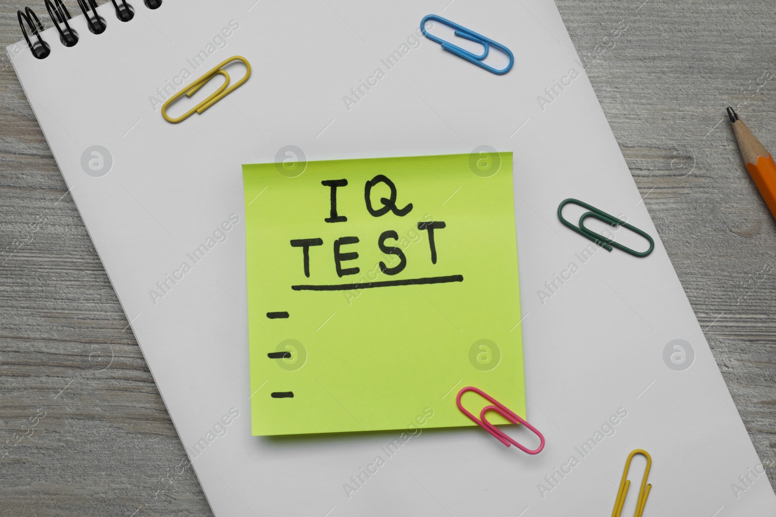 Photo of Sticky paper with words IQ Test, notebook and fasteners on wooden table, flat lay