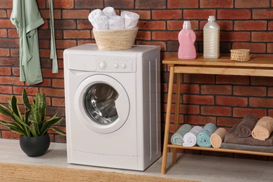 Photo of Washing machine, wooden rack and terry towels indoors. Laundry room interior design