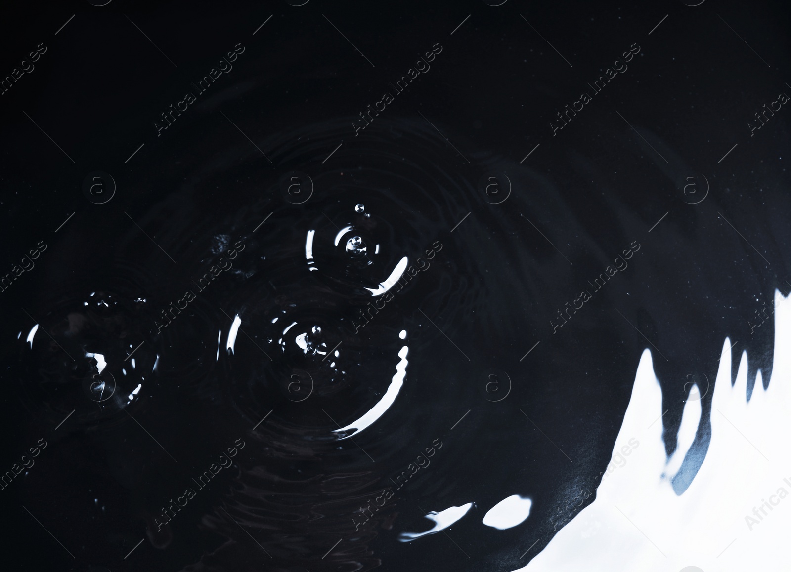 Photo of Rain drops falling down into puddle on dark background, above view