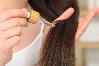 Photo of Woman applying essential oil onto hair on blurred background, closeup