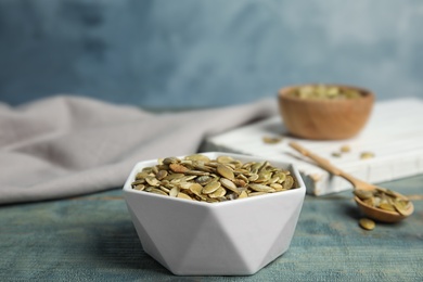 Photo of Bowl of raw pumpkin seeds on blue wooden table