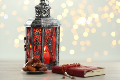 Arabic lantern, Quran, misbaha and dates on table against blurred lights