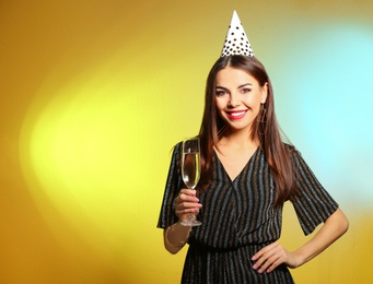 Photo of Portrait of happy woman with party hat and champagne in glass on color background