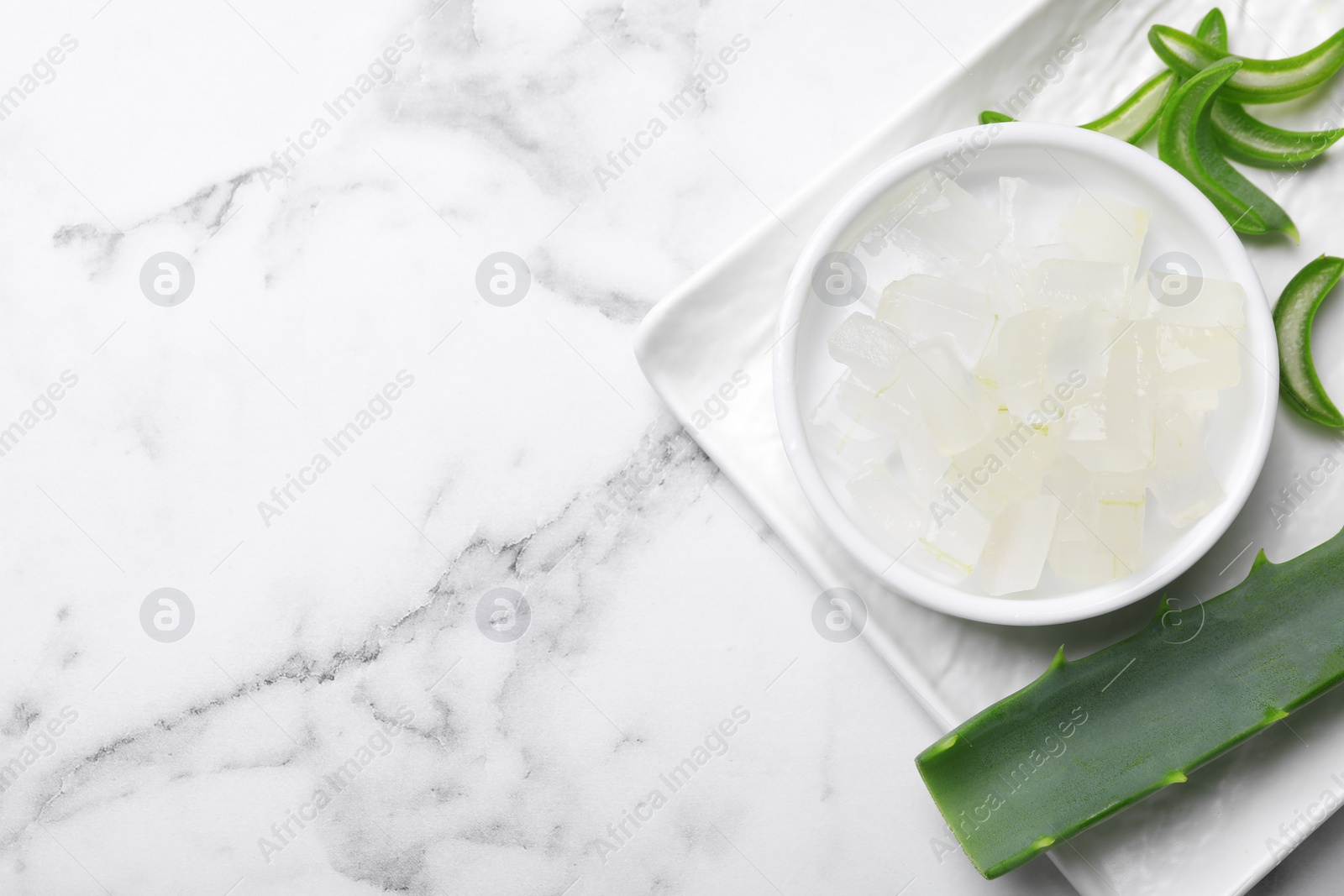 Photo of Aloe vera gel and slices of plant on white marble table, top view. Space for text