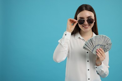 Happy woman with dollar banknotes on light blue background, space for text