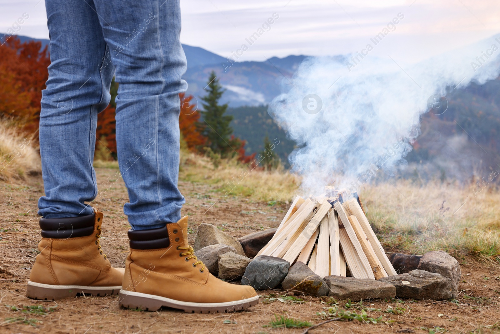 Photo of Man near smoldering bonfire in mountains, closeup. Camping season