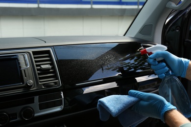 Photo of Man in gloves cleaning car dashboard with disinfectant spray and rag, closeup. Preventive measure during coronavirus pandemic