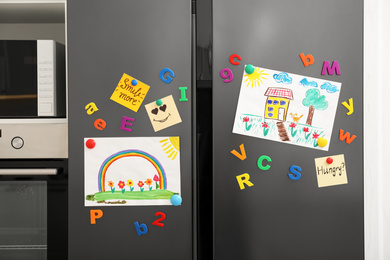 Photo of Modern refrigerator with child's drawings, notes and magnets in kitchen